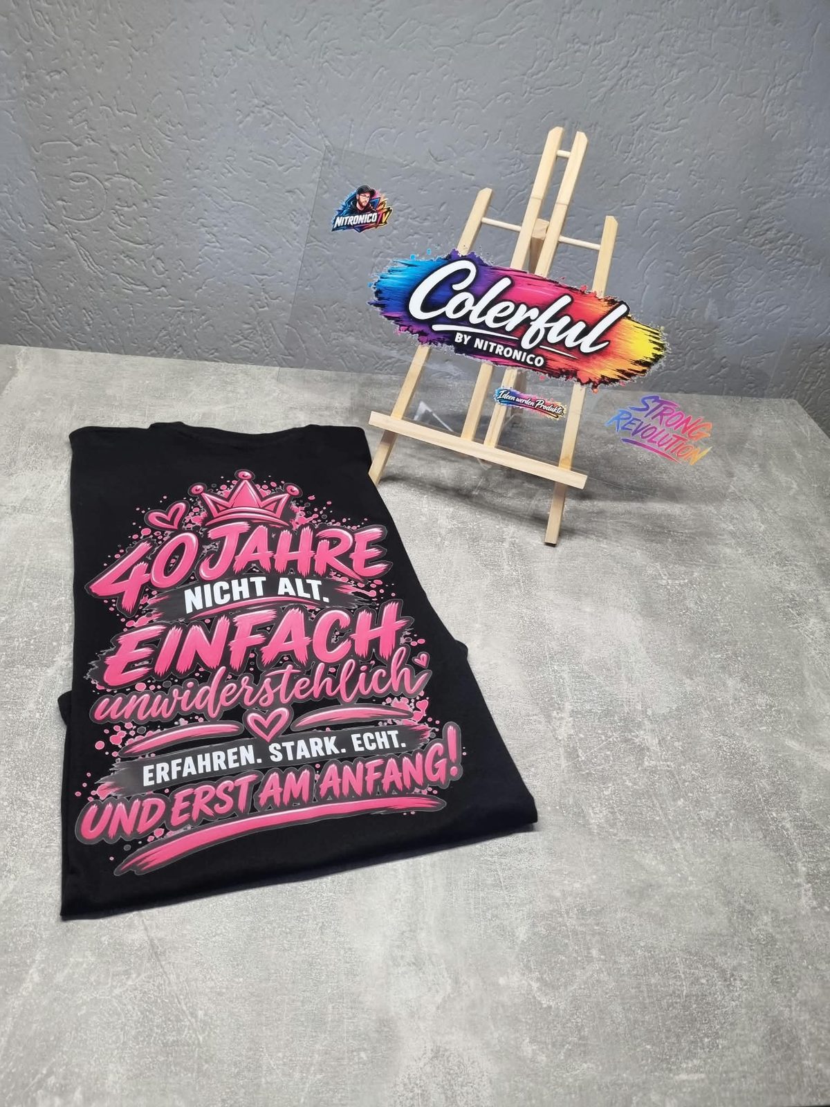 Gefaltetes schwarzes Shirt mit pinkem Rückenmotiv und Colerful-Staffelei